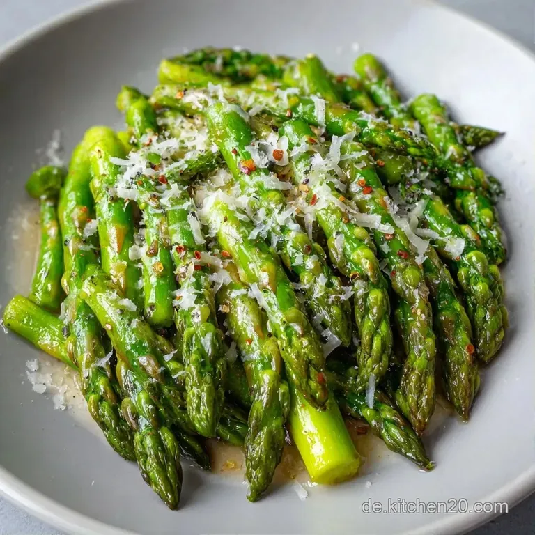 Elegant angerichteter gr&uuml;ner Spargel auf einer dunklen Platte, bestreut mit feinen K&auml;seflocken und frischen Kr&auml;utern.